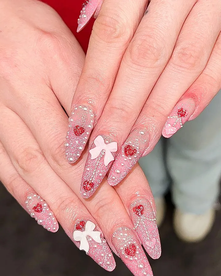 Lange rosa Nägel mit Herzen, Glitzer und einer weißen Schleife